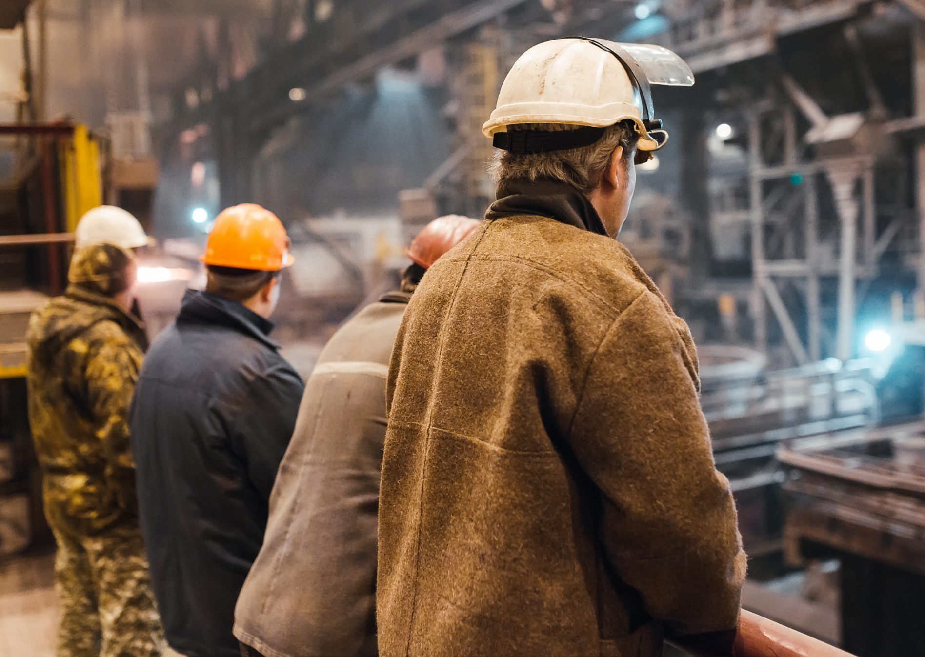 Rückenansicht von Arbeiter in einer Halle mit Sicherheitshelmen